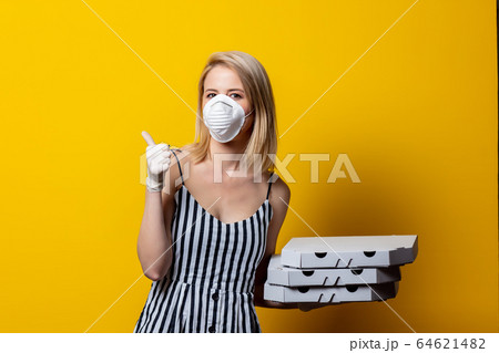 Blonde woman in face mask and gloves holds pizza Blonde woman in face mask and gloves holds pizza 64621482