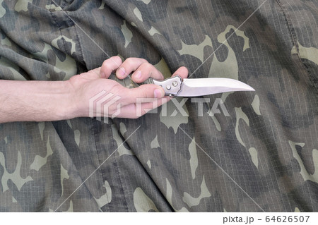 Hand with small knife on camouflage fabric 64626507