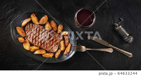Grilled beef steak panorama with baked potato wedges and red wine, shot from above on a dark background 64633244