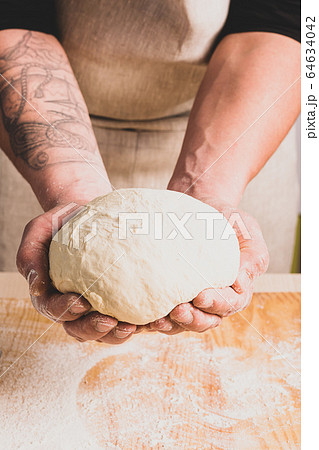 Concept process of making alternative yeast-free home-made bread. A man kneads a kneading pot with dough on the table. 64634042