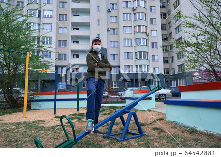 teen boy stands by seesaw on playground near teen boy stands by seesaw on playground near 64642881