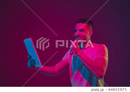 Caucasian man's portrait isolated on pink-purple studio background in neon light, using tablet Caucasian man's portrait isolated on pink-purple studio background in neon light, using tablet 64655973
