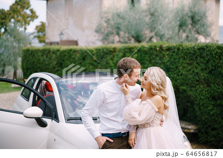 Beautiful bride and groom leaning on a convertible and looking at each other in the Medici Villa of Lilliano Wine Estate, Tuscany, Italy. 64656817