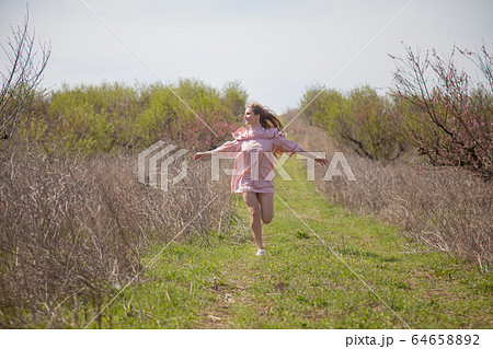 Beautiful blonde woman in pink dress on the road in the garden in the spring 64658892