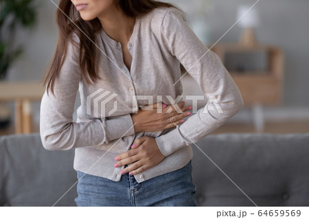 Young sick woman standing holding belly suffering from stomach pain 64659569