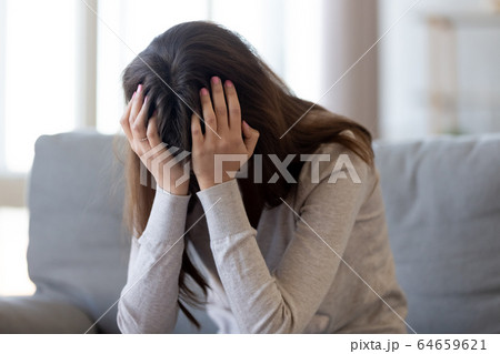 Depressed young woman holding head in hands feeling hurt upset 64659621