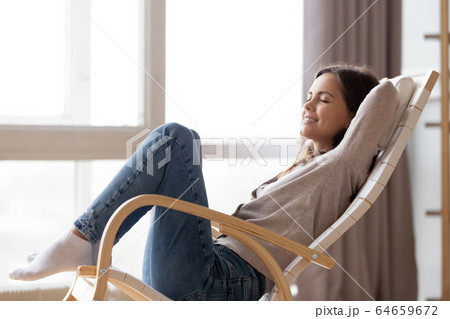 Relaxed calm young woman lounging sitting in comfortable rocking chair 64659672