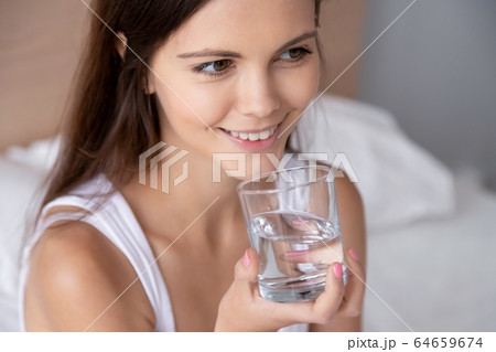 Thirsty young woman holding glass drinking water in bed 64659674