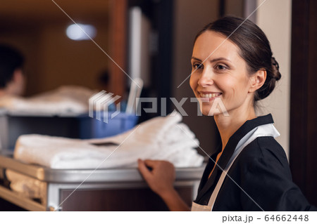A portrait of a housekeeping lady with a cleaning cart and cleaning supplies, looking at the camera and posing 64662448