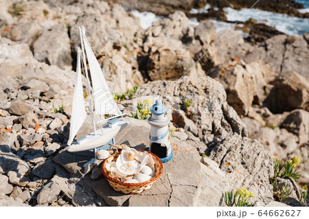 Toy wooden sailing boat and blue lighthouse and seafish plate on the rocky sea beach of the Adriatic Sea in Montenegro Toy wooden sailing boat and blue lighthouse and seafish plate on the rocky sea beach of the Adriatic Sea in Montenegro 64662627