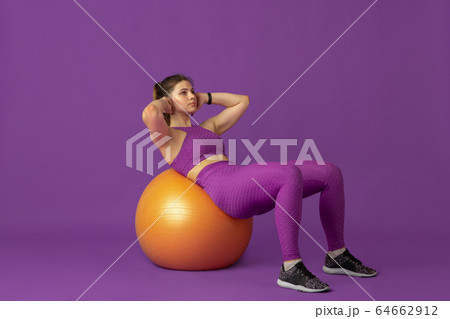 Beautiful young female athlete practicing on purple studio background, monochrome portrait 64662912