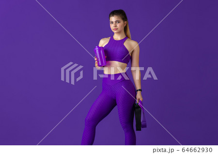 Beautiful young female athlete practicing on purple studio background, monochrome portrait 64662930