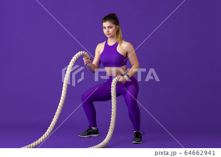 Beautiful young female athlete practicing on purple studio background, monochrome portrait 64662941