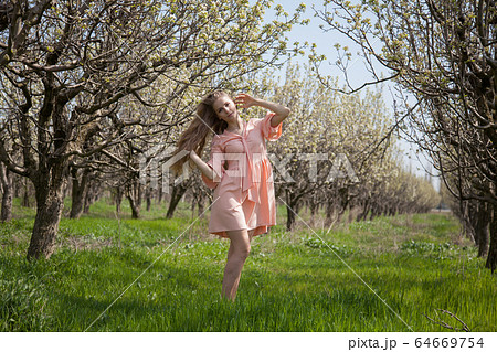 Beautiful blonde woman in pink dress walks through the flowering garden 64669754