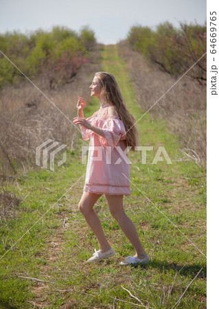 Beautiful blonde woman in pink dress walks through the flowering garden Beautiful blonde woman in pink dress walks through the flowering garden 64669765