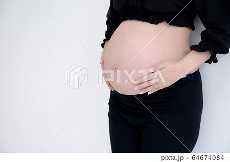 Pregnant woman in black dress and hands hold on belly on a white wall background Pregnant woman in black dress and hands hold on belly on a white wall background 64674084