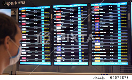 Man in medical masks from coronavirus look at the departure Board at an airport during global pandemic where all flights canceled. Covid-19. 64675873
