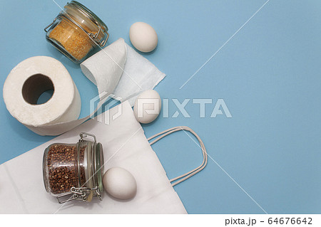 Donation food. Corn grits, eggs,  buckwheat in jar, toilet paper, white bag on blue background. 64676642