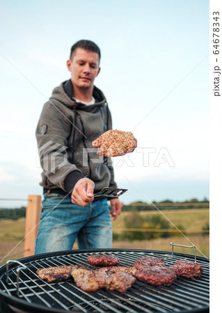 Barbecue grill. A man fries meat steaks and meatballs for hamburgers, turns the meat over with tongs. Barbecue grill. A man fries meat steaks and meatballs for hamburgers, turns the meat over with tongs. 64678343