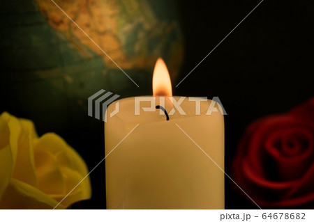 Burning yellow wax candle, globe and roses 64678682