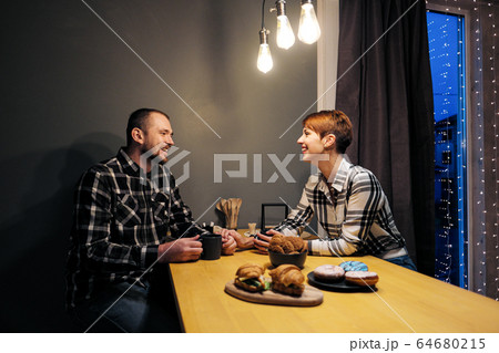 Young married couple in casual clothes, man and woman, sitting at home in the kitchen at the table. Soul communication and home comfort. Young married couple in casual clothes, man and woman, sitting at home in the kitchen at the table. Soul communication and home comfort. 64680215