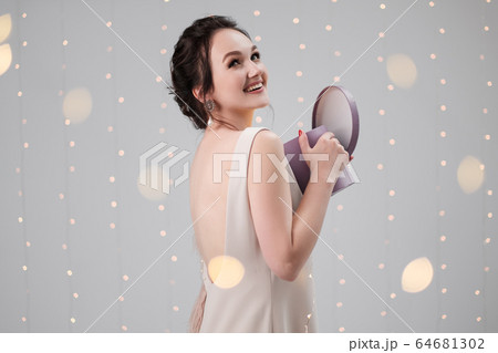Young brunette woman in evening dress on a white background. Holding Christmas present box. Joy, happiness and surprise. 64681302