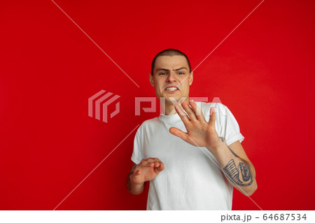 Caucasian young man's portrait on red studio background, emotinal and expressive Caucasian young man's portrait on red studio background, emotinal and expressive 64687534