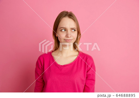 Caucasian young woman's monochrome portrait on pink studio background, emotinal and beautiful 64688895