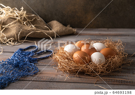 Brown and white chicken eggs in a straw nest on wooden background. Next to eco string bag. Rustic Brown and white chicken eggs in a straw nest on wooden background. Next to eco string bag. Rustic 64693198