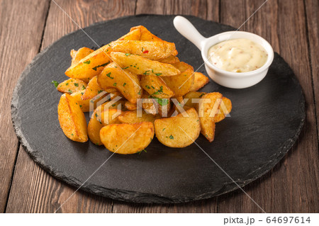 Fried potato wedges on a round black board with mustard sauce. 64697614