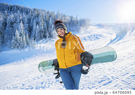 Sporty female holds snowboard in mountains in jeans 64700095