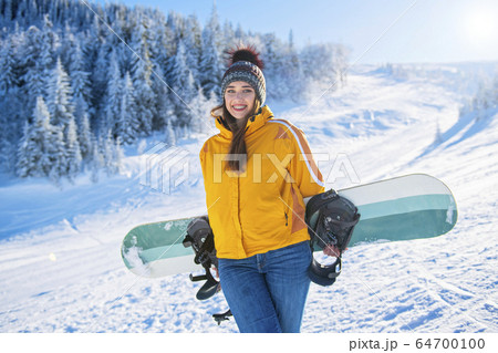 Sporty female holds snowboard in mountains in jeans 64700100