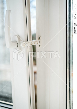 Open white PVC window with a fixing device for ventilation, in natural light. Horizontal photo. 64700289