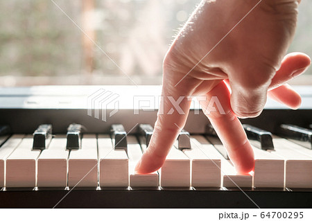 Fingers press the keys of the piano, as if legs were walking, in natural light from the window. 64700295