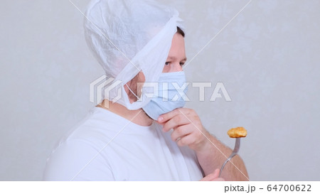 bearded man in a bag on his head and a protective mask has a cutlet from a fork. Fear of infection 64700622