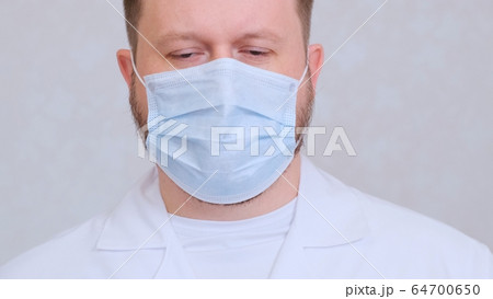 sad and upset Male in a protective mask and a white shirt looks at the camera, close-up. Hygiene sad and upset Male in a protective mask and a white shirt looks at the camera, close-up. Hygiene 64700650