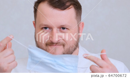 bearded male doctor is trying to put on a protective mask and get mad at her. Hygiene concept 64700672