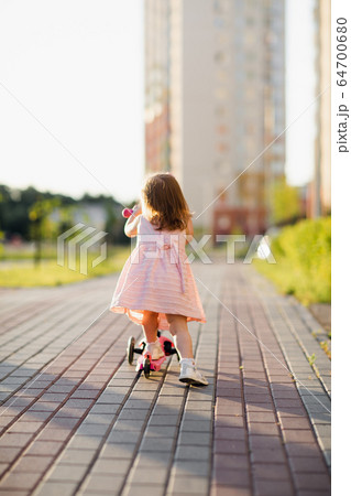 Little girl wearing dress riding scooter outdoors 64700680