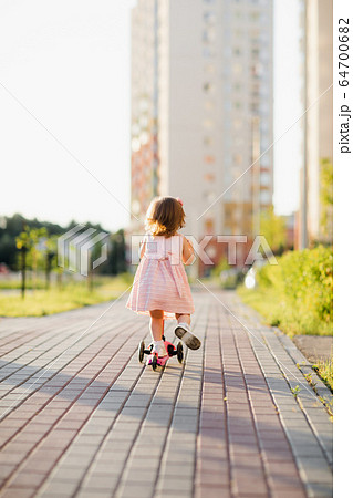 Little girl wearing dress riding scooter outdoors 64700682