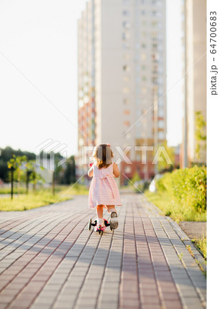 Little girl wearing dress riding scooter outdoors 64700683