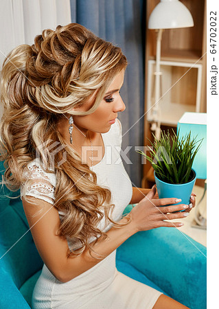 girl in a luxurious white dress sitting on a soft armchair holds in her hands green flower in a pot girl in a luxurious white dress sitting on a soft armchair holds in her hands green flower in a pot 64702022