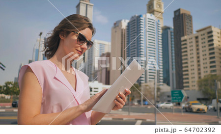 A girl works on a tablet against the background of skyscrapers of a metropolis. A girl works on a tablet against the background of skyscrapers of a metropolis. 64702392