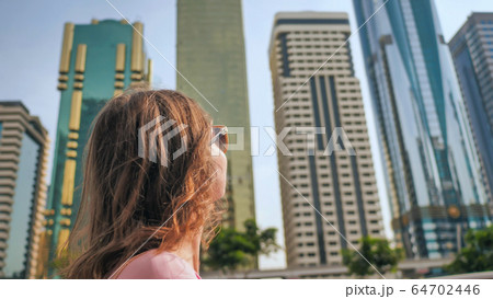 Happy girl walks in the center of Dubai against the background of skyscrapers. 64702446