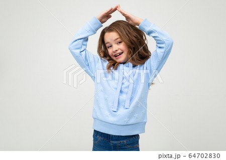 smiling teenage girl in casual blue hoodie put her hands over her head in the form of a roof on a 64702830