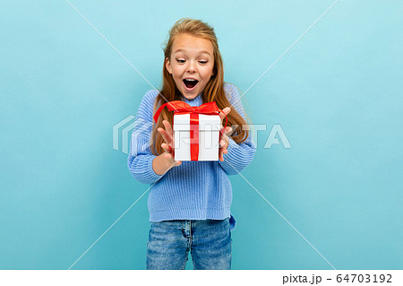 surprised european girl holding a gift on a light blue background 64703192
