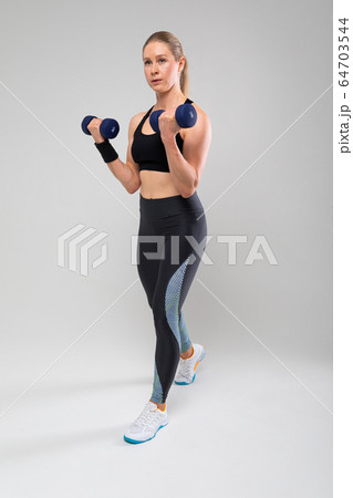 slim fit blonde girl in a sports uniform is engaged in physical exercises on a gray background 64703544