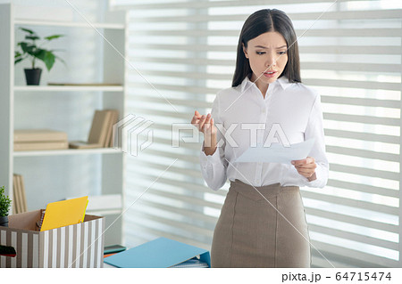 Upset young brunette female holding piece of paper, reading it 64715474