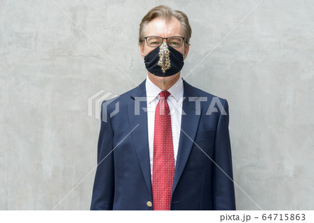 Mature businessman in suit with mask for protection from corona virus outbreak against concrete wall Mature businessman in suit with mask for protection from corona virus outbreak against concrete wall 64715863