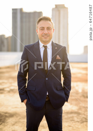 Happy mature handsome businessman in suit against view of the city Happy mature handsome businessman in suit against view of the city 64716487