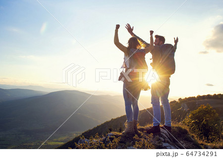 happy couple man and woman tourist at top of mountain at sunset outdoors during a hike in summer 64734291
